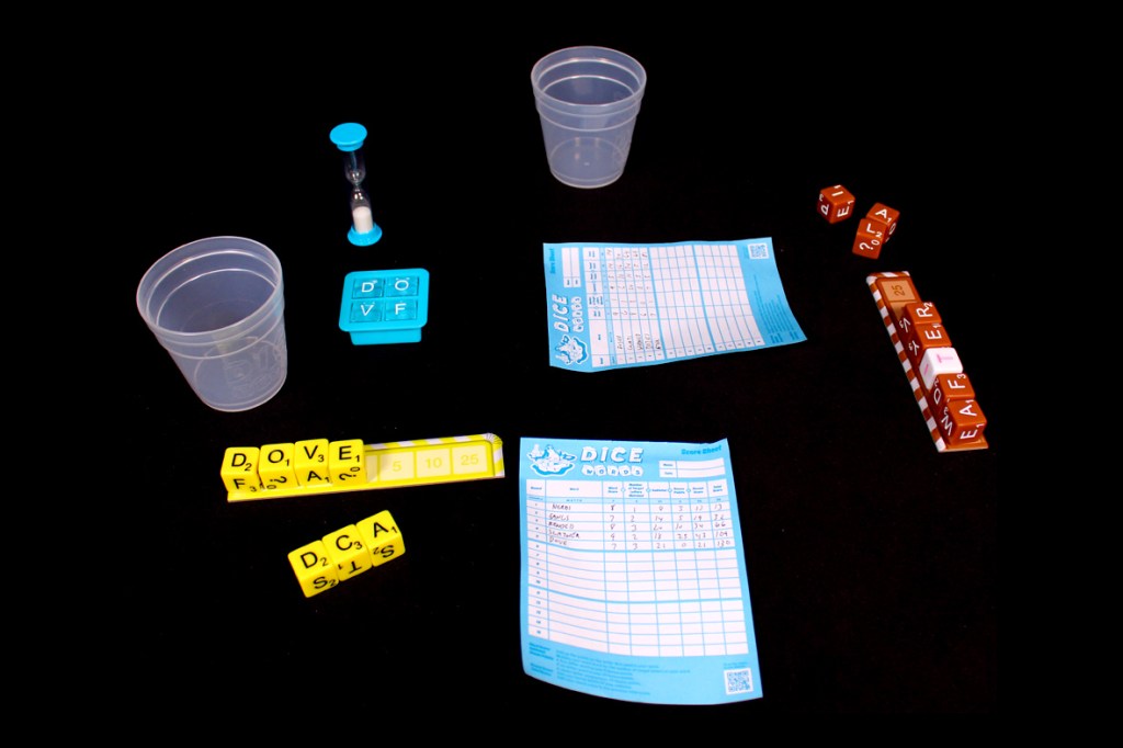 An arrangement of game components for Dice Words including score sheets, plastic cups, a timer, alphabet dice, and a scoring tray on a black background.