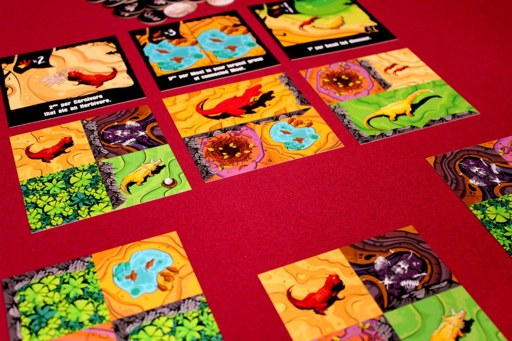 A tabletop game layout featuring colorful cards depicting dinosaurs and landscapes, along with scoring indicators, on a red playing surface.
