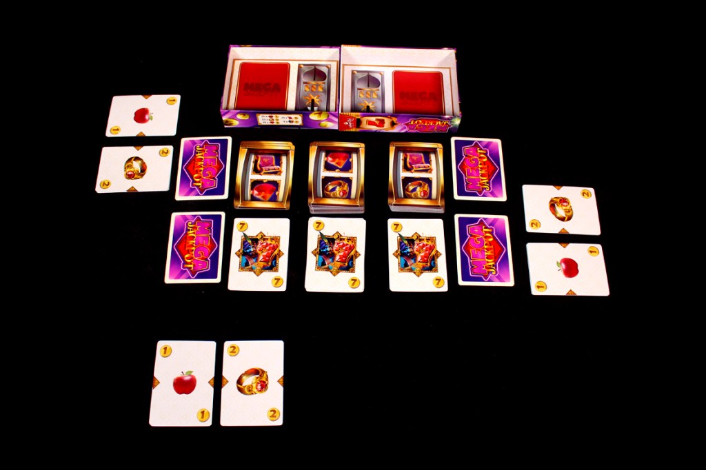 An overhead view of the Mega Jackpot board game setup, featuring several playing cards with graphics related to jackpots, along with the game's box displayed at the top.