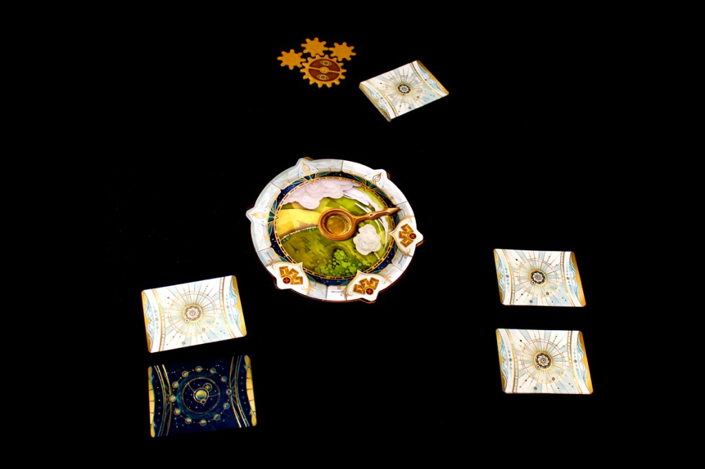 A tabletop game setup featuring a circular game board with a clock hand and several playing cards arranged around it on a black background.