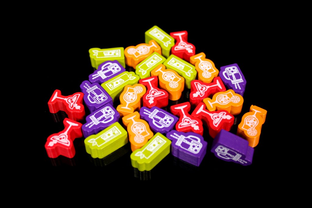 Colorful cocktail tokens in various shapes, including drinks and bar equipment, scattered on a black surface.