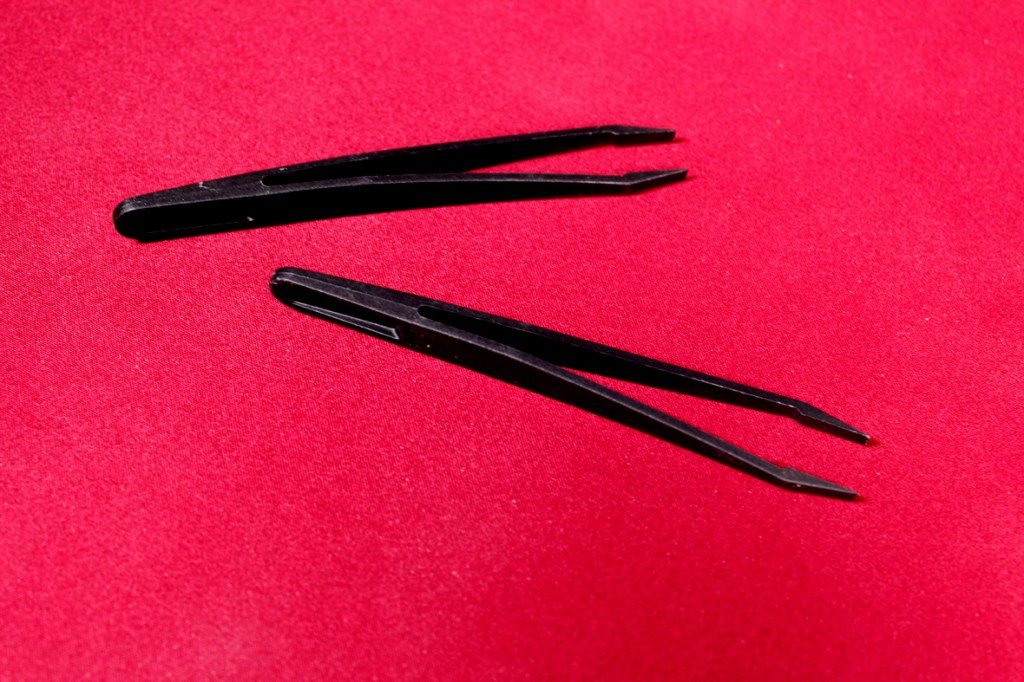 Two black tweezers resting on a red surface.
