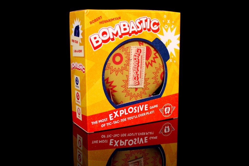 A close-up of the packaging for the board game Bombastic, featuring bright colors and bold text that emphasizes it as an explosive version of tic-tac-toe. The box includes images and text indicating the number of players, approximate playtime, and game details.