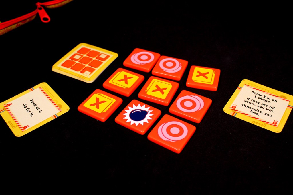 A layout of game components from Bombastic, including a 3x3 grid of tiles showing Xs, Os, and a bomb, along with action cards that explain gameplay mechanics.