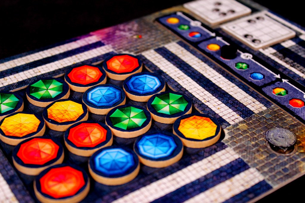 Close-up of a colorful board game player board with various hexagonal tokens in red, blue, green, yellow, and orange arranged on a grid.