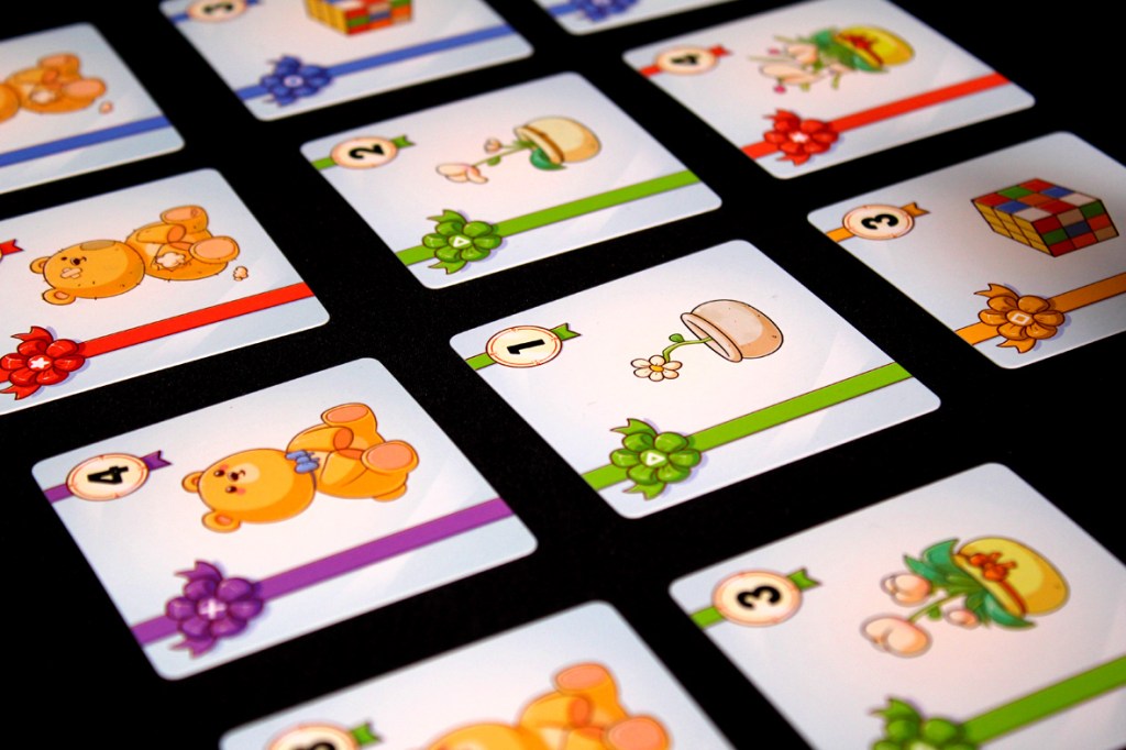 A close-up of colorful game cards featuring cute illustrations of teddy bears, gifts, and flowers, each adorned with colored ribbons and numbers.