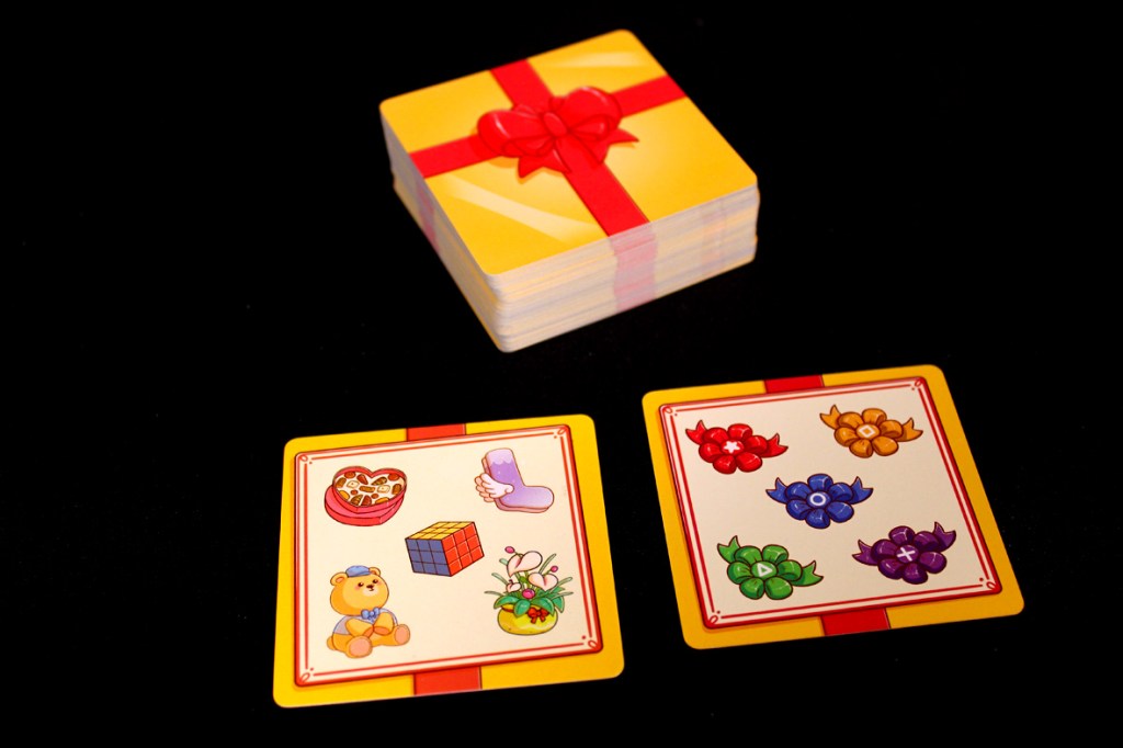A stack of gift-themed cards is displayed on a black background, with two opened cards featuring colorful illustrations of toys and flowers.