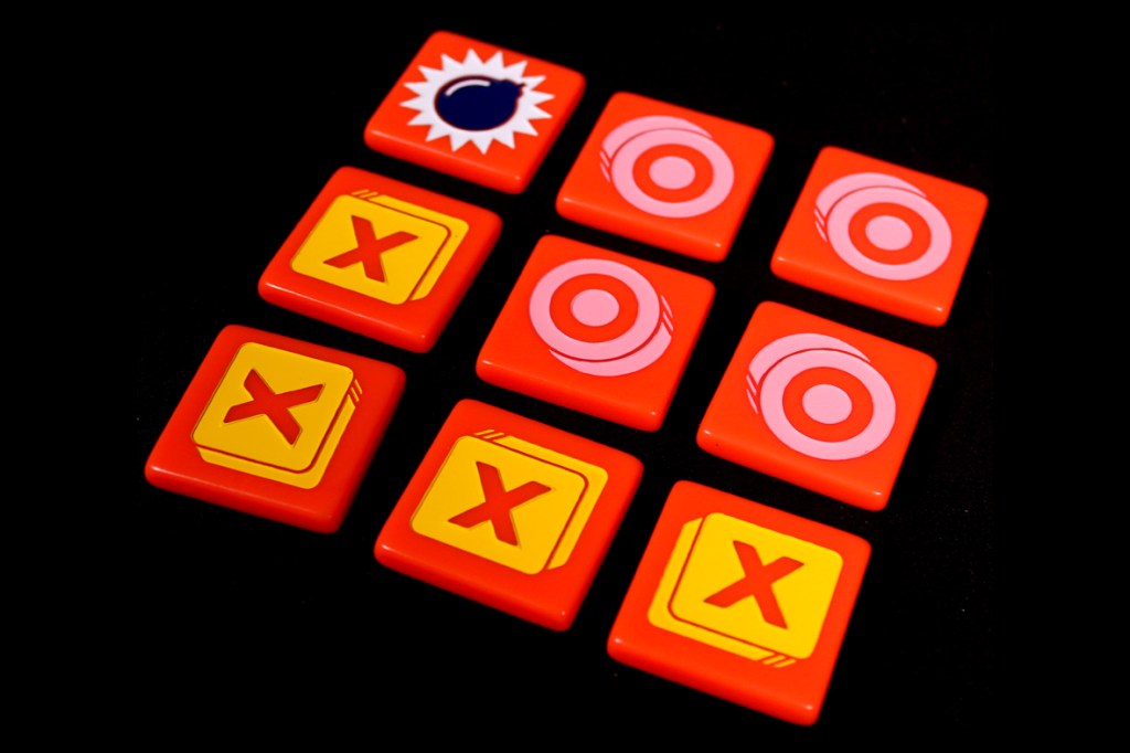 A 3x3 grid of game tiles featuring bombs, Xs, and circular targets on a red background.