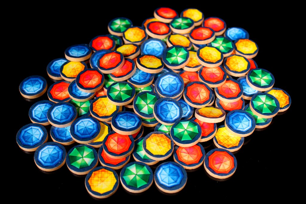 A pile of colorful game tokens featuring various designs, including blue, green, red, and yellow circles with geometric patterns, set against a black background.