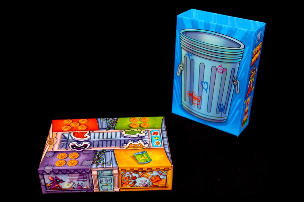 An illustrated game box for Super Meow featuring colorful graphics of cats and playful designs, alongside a blue trash can-themed box.