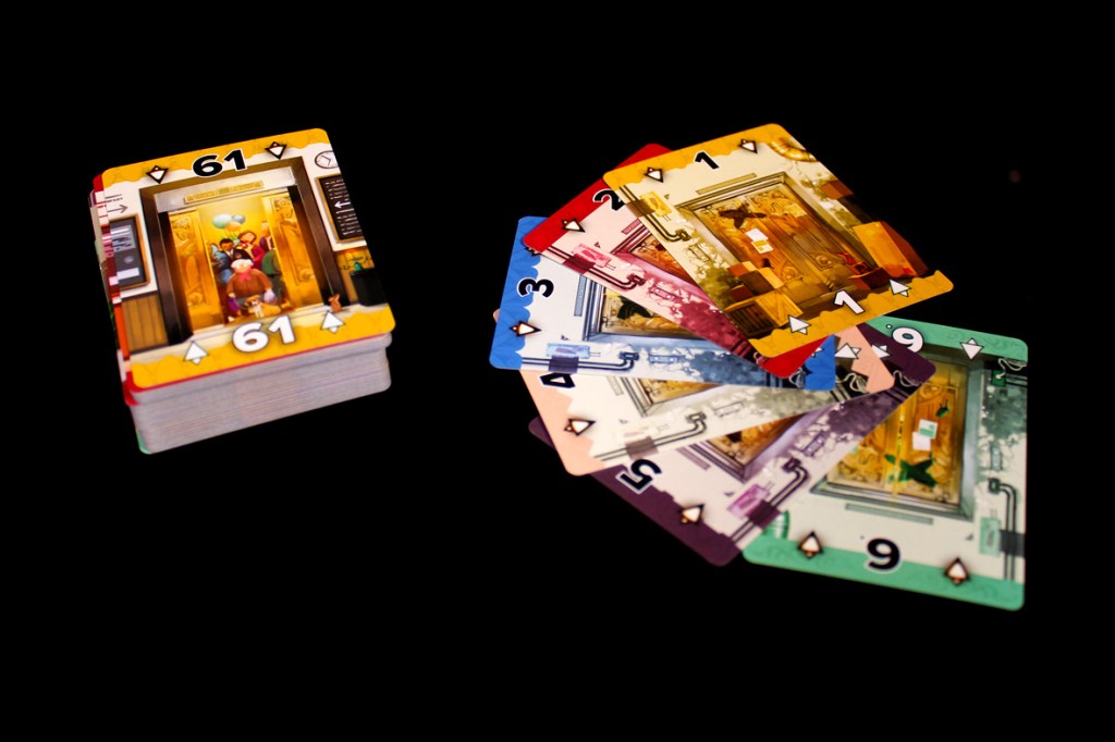 A stack of colorful playing cards featuring an elevator scene on the top card, with additional cards scattered beside it showing various numbered doors.