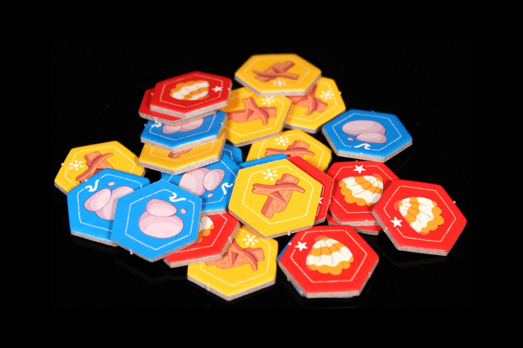 A collection of colorful hexagonal game tokens with various illustrated designs, including farming items and food symbols, scattered on a black background.