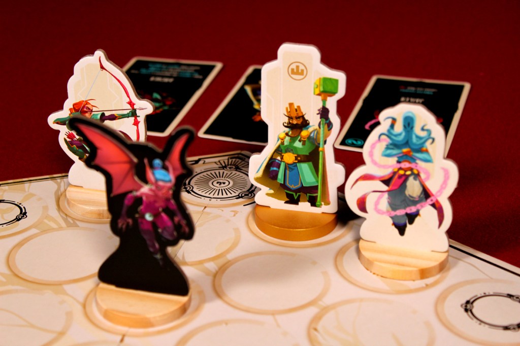 A tabletop game scene featuring colorful character standees, including an archer, a wizard, and a bat-like creature, set against a red backdrop with game cards and a game board visible.