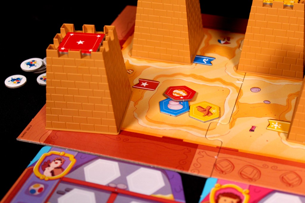 A colorful board game setup featuring two sandcastle structures, various tokens, and game tiles depicting a sandy landscape.