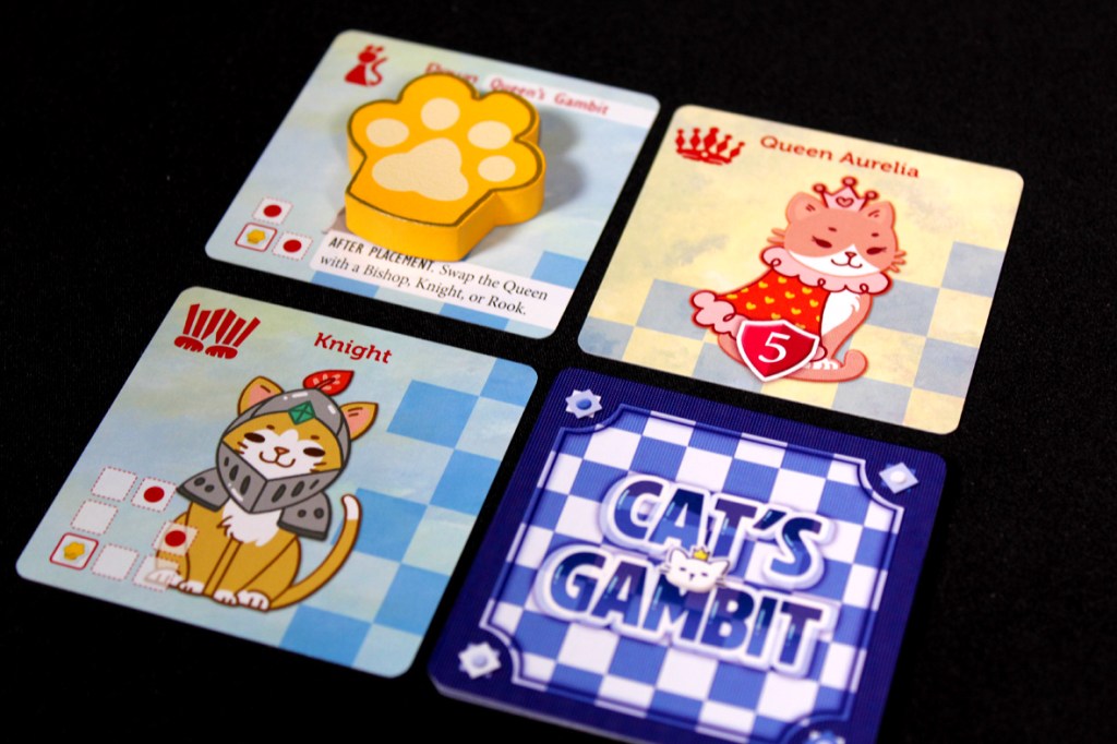 A collection of game cards from Cat's Gambit: Queen Aurelia, featuring a cute cat Knight character, the card for Queen Aurelia, a paw token, and the game's title card. The cards are placed against a black background.