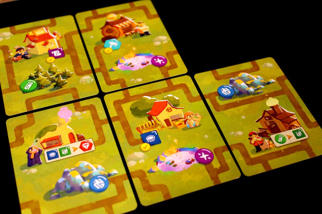 Top-down view of game cards for 'A Dragon's Gift' featuring various village structures, resources, and pathways.