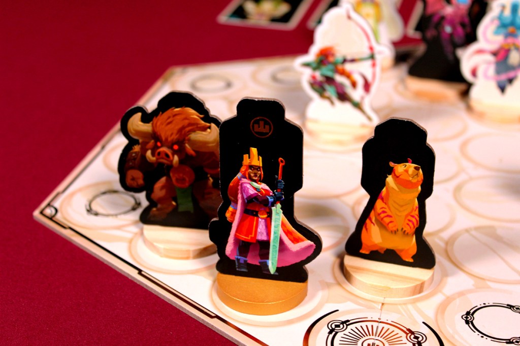 A colorful board game setup featuring three character game pieces: a warrior in a crown holding a sword, a bull-like creature, and a tiger-like character, positioned on a geometric board.