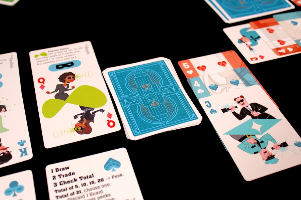 A close-up view of a tabletop card game featuring multiple illustrated playing cards with characters and game instructions, set against a black surface.