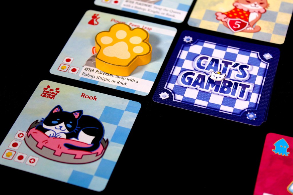 Close-up of game cards from 'Cat's Gambit' featuring a cat illustration, a paw piece, and game instructions.
