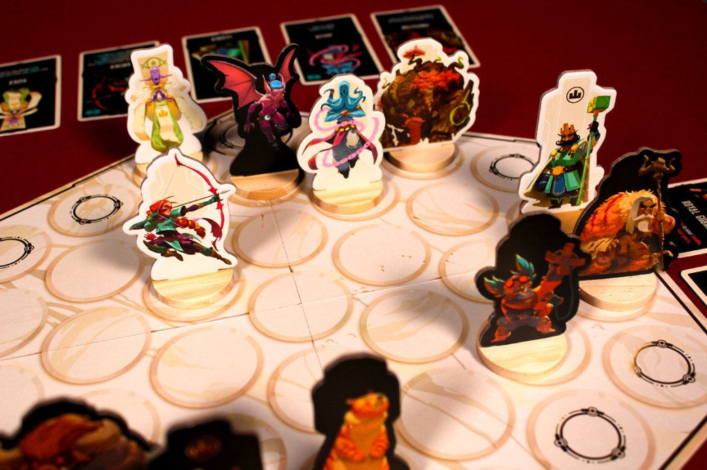 A tabletop game scene featuring various character tokens on a circular grid, with several cards visible in the background. The tokens display colorful and stylized designs, showcasing different fantasy characters.