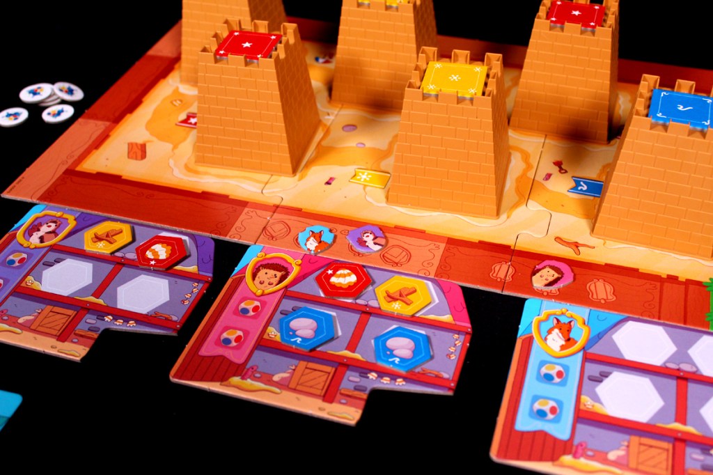 Colorful board game setup featuring sandcastle pieces and character cards with various tokens and shapes.