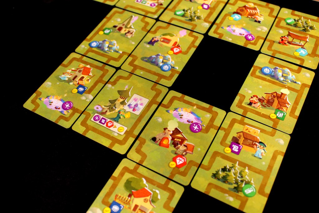 A layout of game cards depicting a village, including various buildings, resources, and paths connecting them, showcasing a whimsical art style.