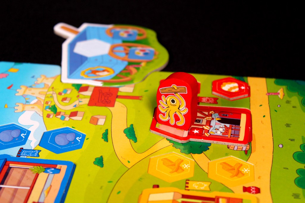 Close-up of a colorful board game featuring a path through a cartoon landscape, with tokens and game pieces including a red octopus and various symbols.