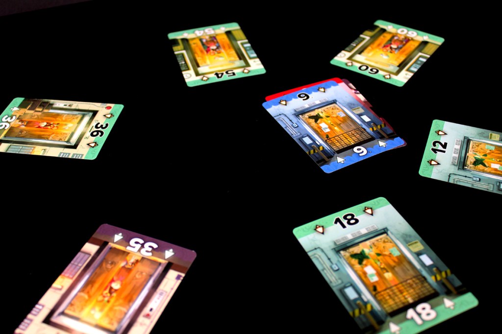 A flat lay image of multiple playing cards spread out on a black surface, featuring illustrated elevators and numbers ranging from 9 to 36.