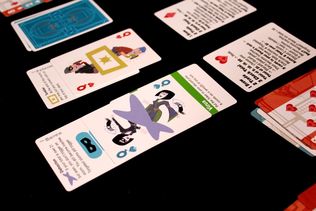 A collection of playing cards displayed on a black surface, featuring various illustrations and text, including characters like 'The Raven' and 'Vitus'.