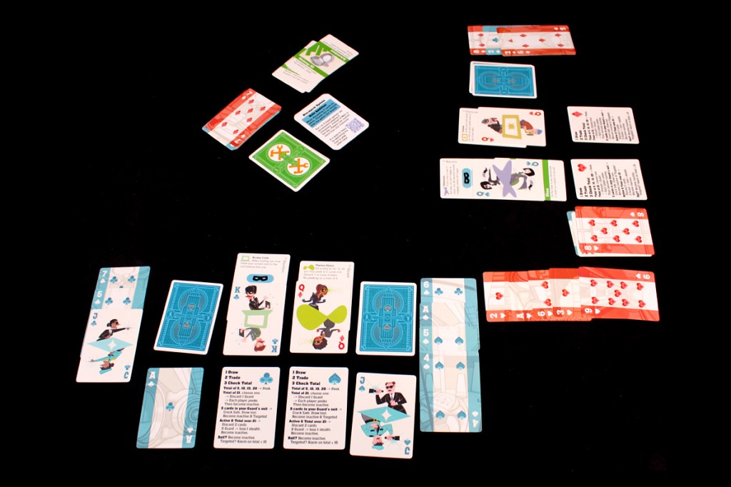 A tabletop scene featuring a variety of colorful playing cards arranged on a black surface, including character illustrations and gameplay instructions.