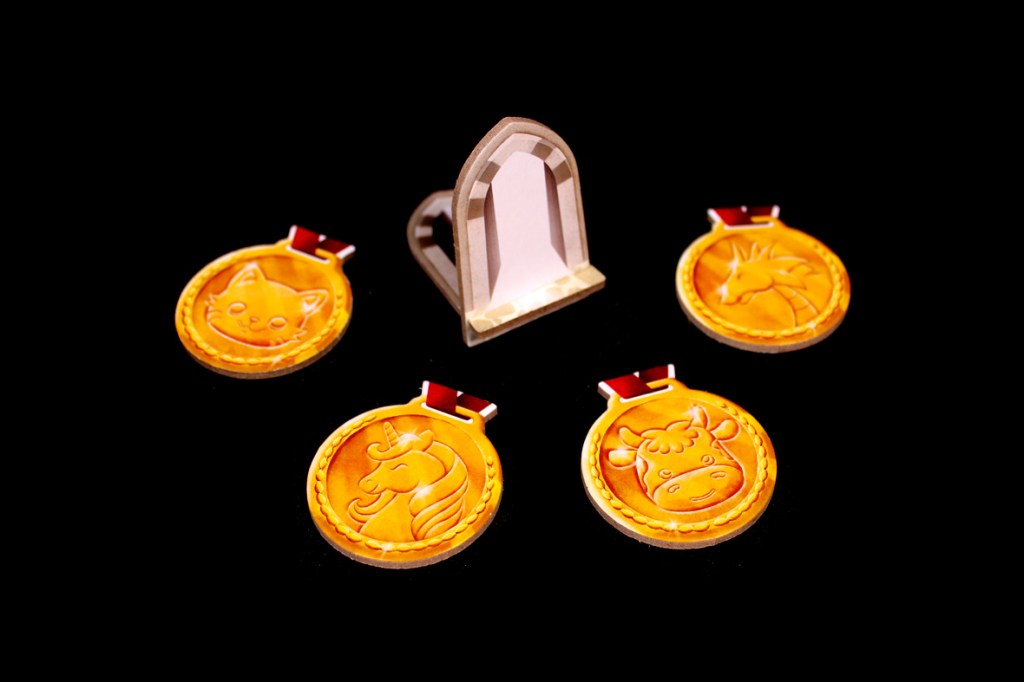 A collection of four round, gold-colored medals featuring animal designs, including a cat, unicorn, and cow, with a decorative arch in the center. The background is black.