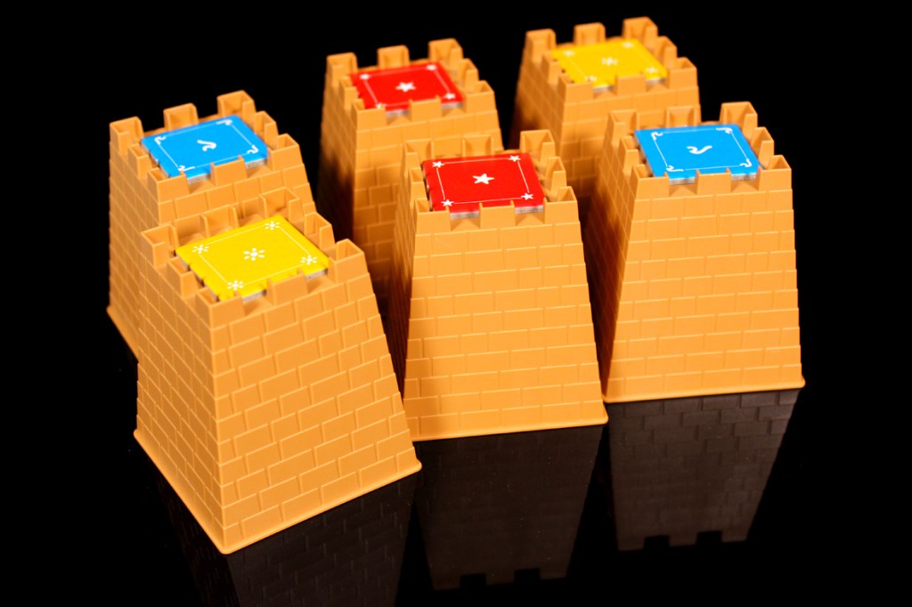 Five colorful castle-shaped game pieces with various symbols on top, set against a black background.