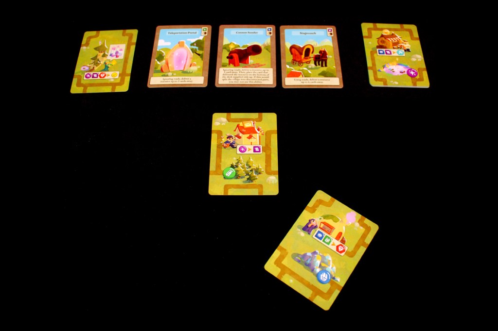 A tabletop game setup featuring cards arranged on a dark surface, including a Teleportation Portal, Commoner, and Magnematch cards, with a central card depicting a scene of crafting in a village.