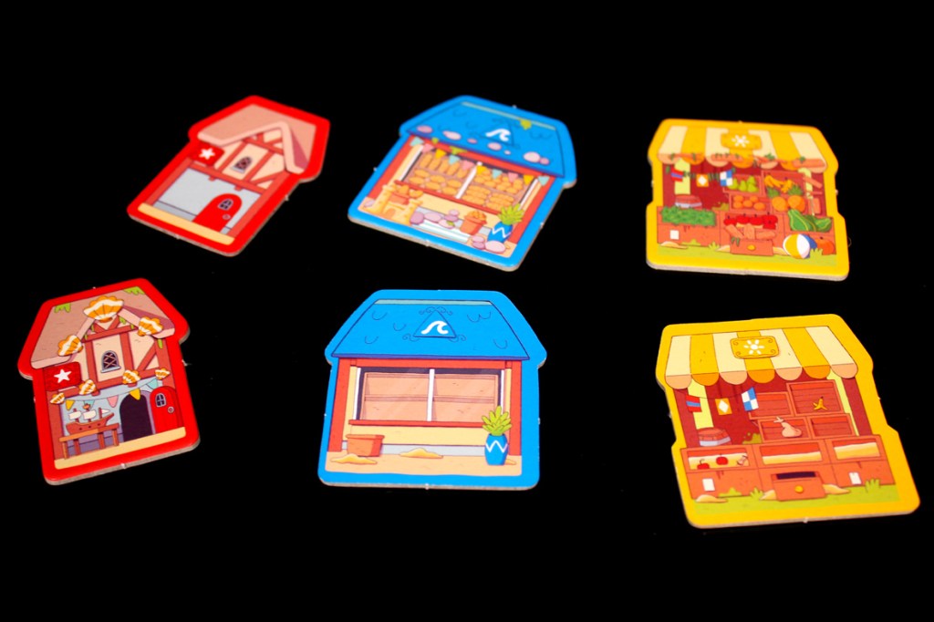 Colorful game pieces shaped like houses and shops, featuring various designs and details, arranged on a black background.