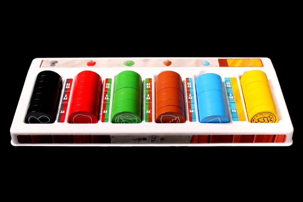 A colorful gaming piece set consisting of cylindrical tokens in black, red, green, brown, blue, and yellow, arranged on a white tray with various symbols and progress indicators.