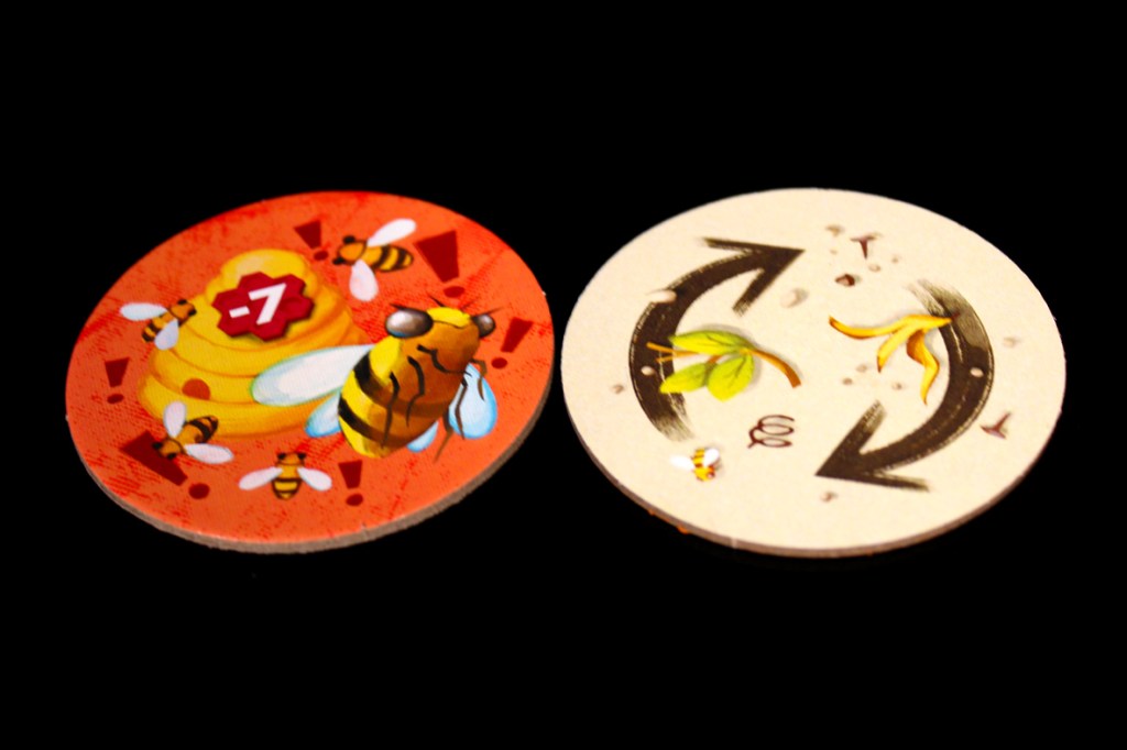 Two round game tokens: one featuring a bee and honeycomb with a '-7' icon, and the other depicting a rotation symbol with flowers and a bee.