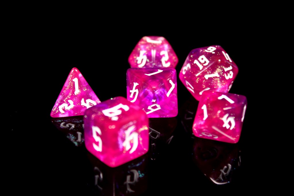 A set of pink, translucent gaming dice with white numbers, including a d20, d12, d10, d8, d6, and d4, on a reflective black background.