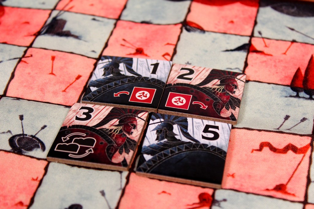 A close-up view of four game tiles on a patterned board, depicting various symbols and numbers, including strategic elements and warrior designs.