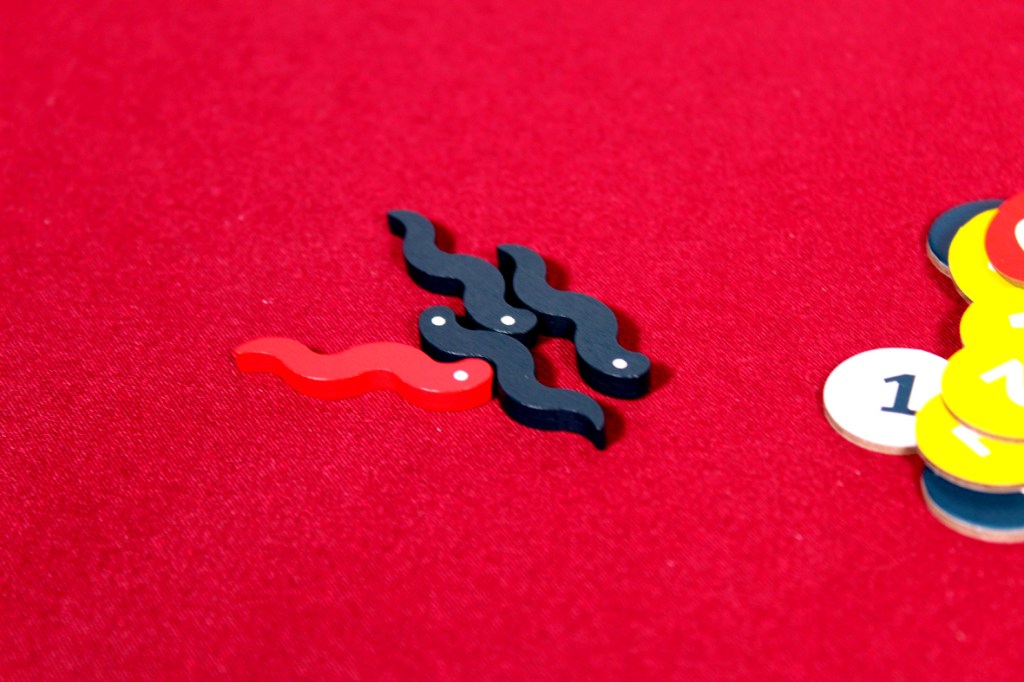 Colorful game pieces shaped like squiggly lines, featuring red and black pieces on a red tablecloth next to numbered tokens.