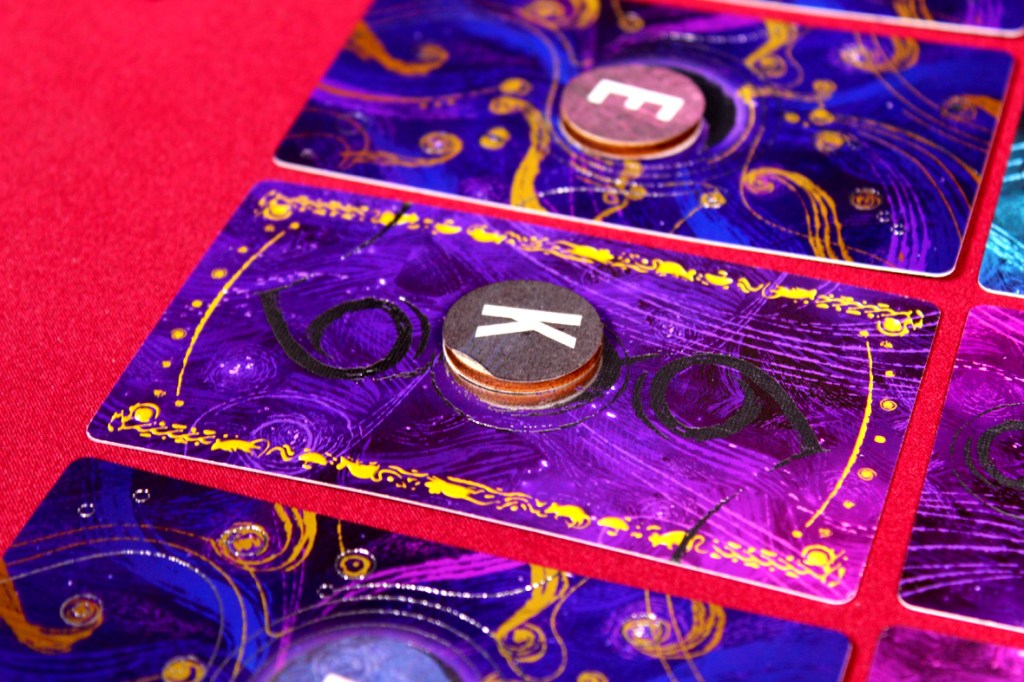 A close-up of colorful game cards featuring artistic purple designs and letters E and K, arranged on a red surface.