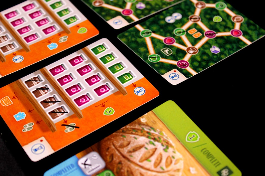 A close-up of various game cards arranged on a dark surface, featuring colorful icons and game mechanics, including resource management and completed tasks.