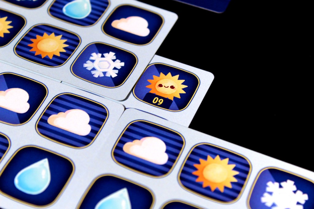 A close-up view of a board game showing various weather-related icons, including the sun, clouds, snowflakes, and water droplets, arranged in a grid pattern.
