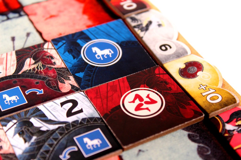 Close-up of a board game layout featuring colorful tiles with various symbols, numbers, and artwork, including a blue horse icon and a red number tile.