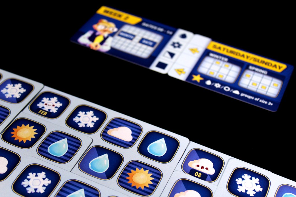 A close-up of a board game featuring a grid with various weather icons, including snowflakes, suns, and clouds, alongside a player reference card showing game days.