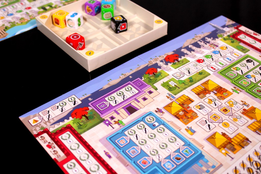 Close-up view of a colorful board game layout featuring various game pieces and dice. The board includes different sections with illustrations and icons, indicating various gameplay elements.