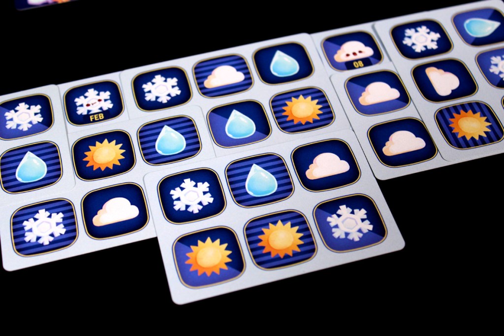 A close-up view of a board game with weather-themed icons, including snowflakes, raindrops, clouds, and suns, arranged in a grid pattern.