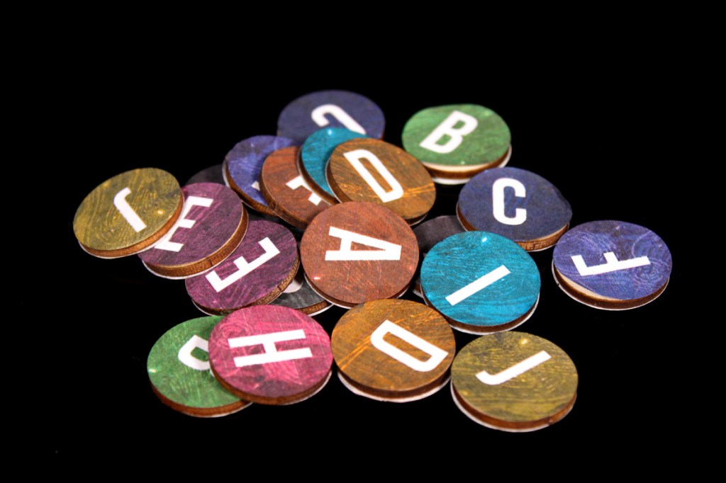 A collection of colorful wooden discs featuring white letters scattered on a black background.