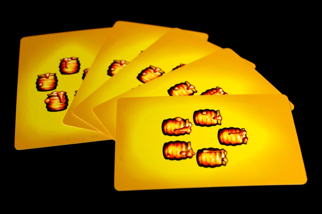 A set of yellow playing cards featuring illustrated images of honeypots arranged on them.