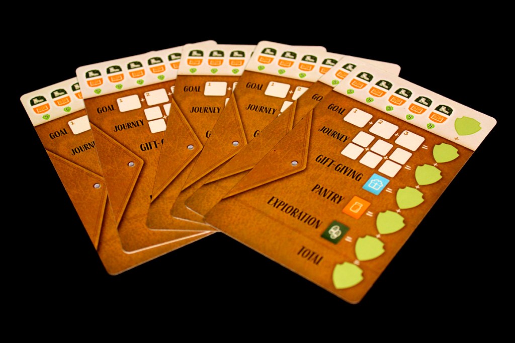 A close-up of several game scorecards featuring sections for tracking goals, journeys, gift giving, pantry items, exploration, and total scores, set against a black background.