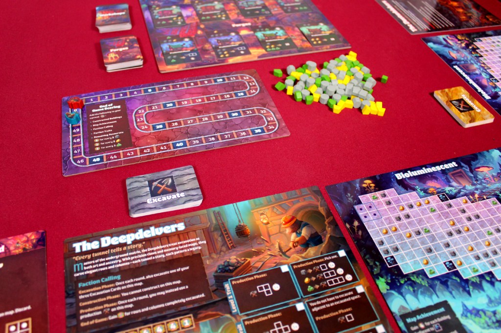 A tabletop board game setup featuring various game components including player boards, cards, and tokens in shades of gray, green, and yellow, placed on a red tablecloth.